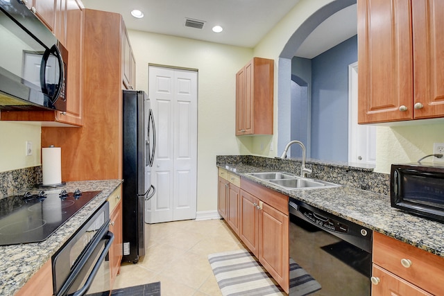 kitchen featuring sink, light tile patterned floors, black appliances, and dark stone countertops