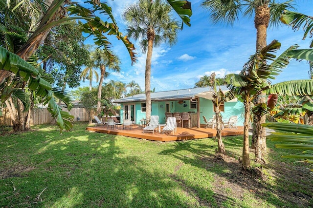 rear view of property with a deck, fence, a lawn, and metal roof