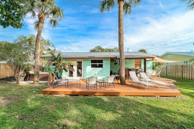 back of property with a hot tub, stucco siding, a lawn, metal roof, and a fenced backyard