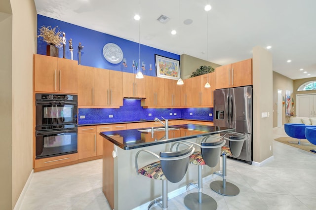 kitchen featuring hanging light fixtures, sink, a kitchen island with sink, black appliances, and a breakfast bar