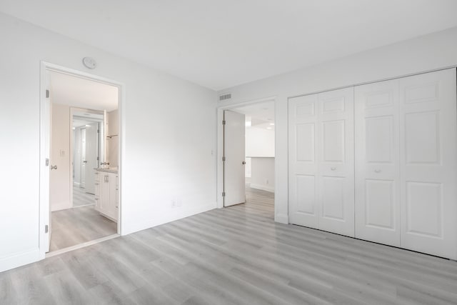 unfurnished bedroom with light hardwood / wood-style flooring, connected bathroom, and a closet