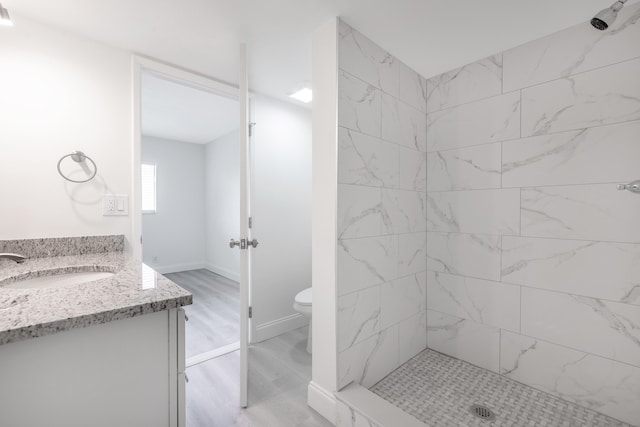 bathroom with a tile shower, hardwood / wood-style floors, vanity, and toilet