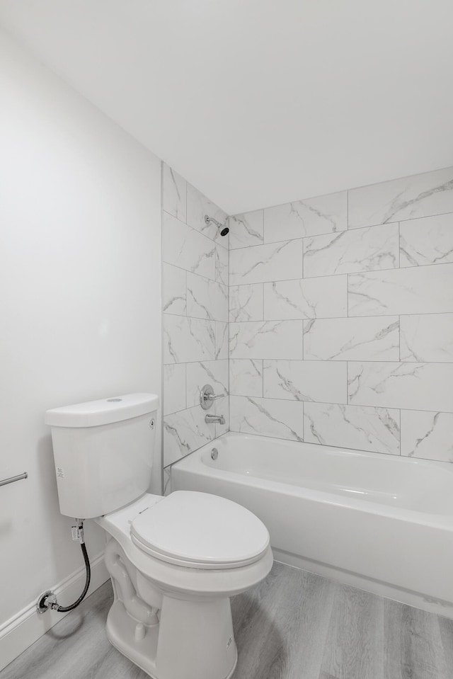 bathroom with wood-type flooring, tiled shower / bath, and toilet