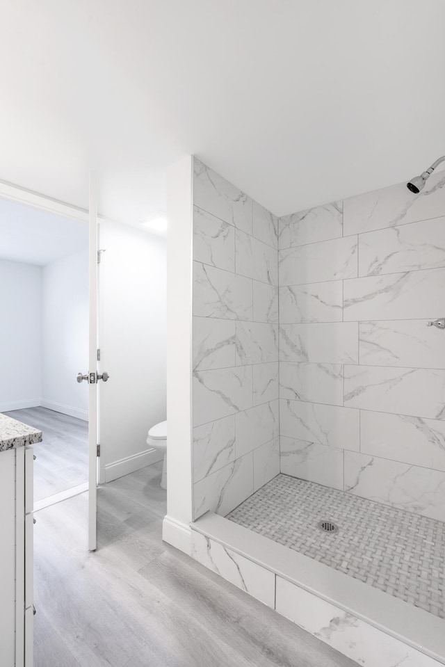 bathroom with a tile shower, wood-type flooring, vanity, and toilet