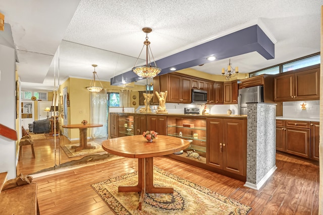 kitchen featuring stainless steel appliances, a textured ceiling, hardwood / wood-style flooring, crown molding, and decorative light fixtures