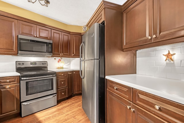 kitchen featuring stainless steel appliances, a textured ceiling, light hardwood / wood-style flooring, and backsplash