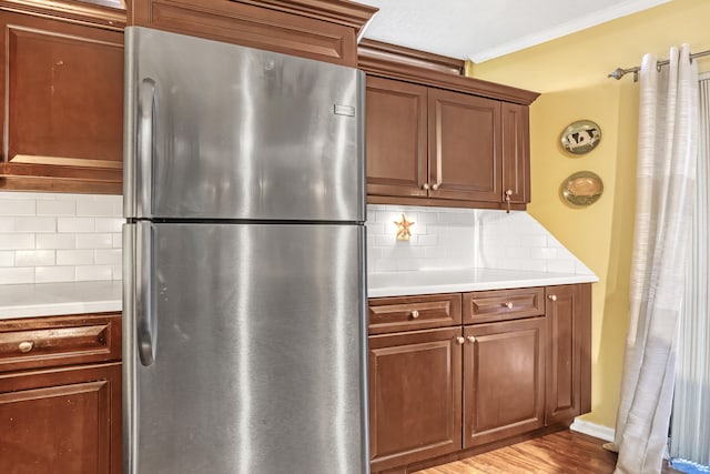 kitchen with light hardwood / wood-style floors, stainless steel fridge, backsplash, and crown molding