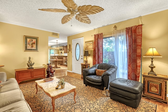 living room featuring ceiling fan, wood-type flooring, ornamental molding, and a textured ceiling