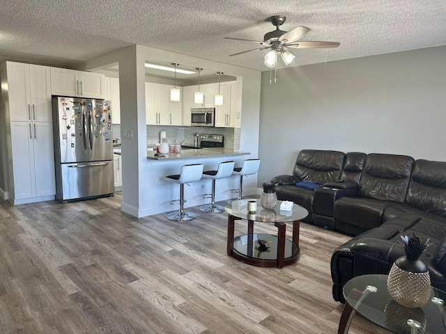 living room featuring a textured ceiling, ceiling fan, and light hardwood / wood-style floors