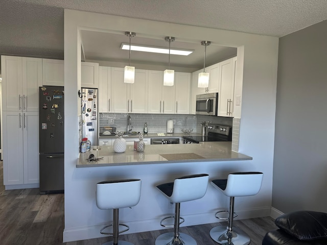 kitchen with pendant lighting, dark hardwood / wood-style flooring, appliances with stainless steel finishes, and white cabinetry