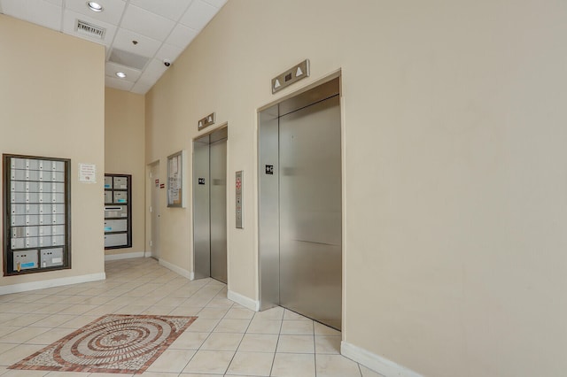 hall with a drop ceiling, light tile patterned flooring, a towering ceiling, and elevator