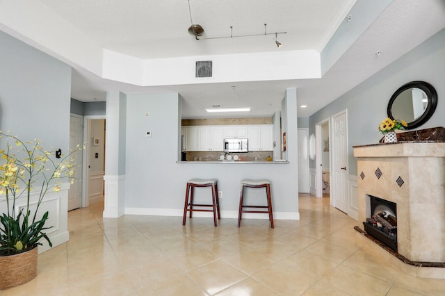 kitchen featuring kitchen peninsula, a tiled fireplace, white cabinetry, a tray ceiling, and a breakfast bar