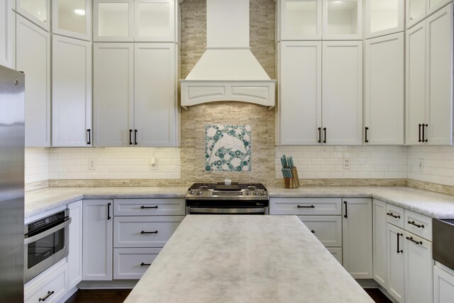 kitchen featuring sink, premium range hood, appliances with stainless steel finishes, backsplash, and a center island