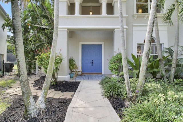 view of exterior entry with fence, a balcony, and stucco siding