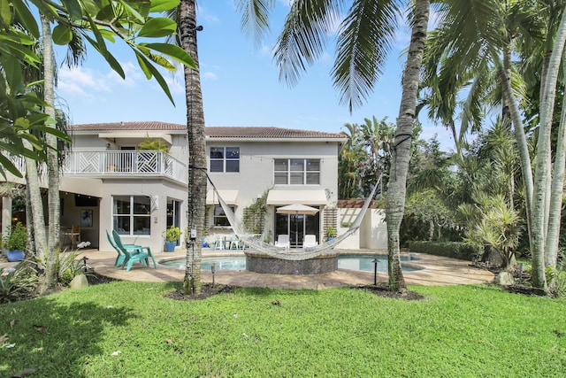 rear view of property with a balcony, a patio area, and a lawn