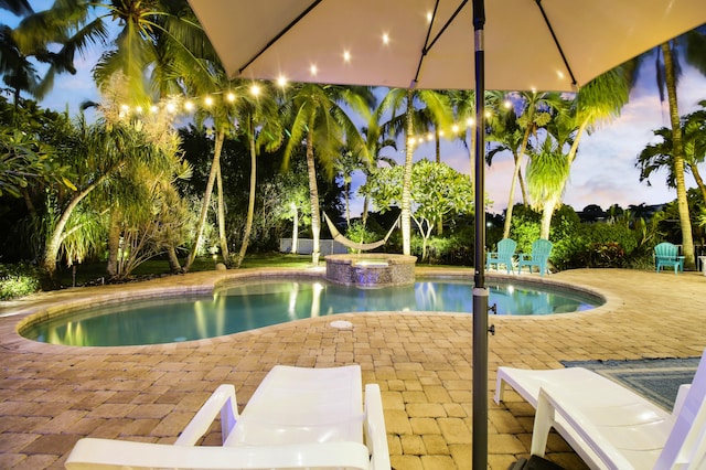 pool at dusk featuring an in ground hot tub and a patio area