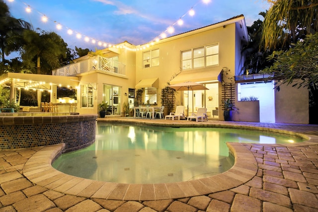 back house at dusk with a balcony and a patio area