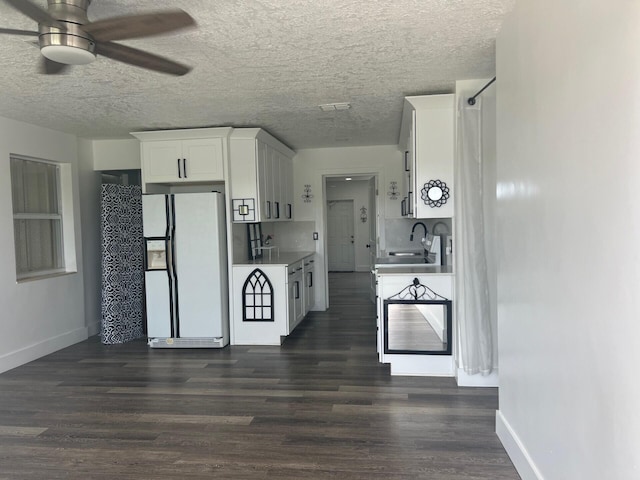 kitchen featuring white refrigerator with ice dispenser, white cabinetry, dark wood-type flooring, ceiling fan, and a textured ceiling