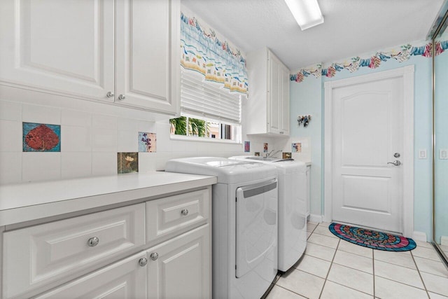 laundry area with cabinets, a textured ceiling, light tile patterned floors, and washing machine and clothes dryer