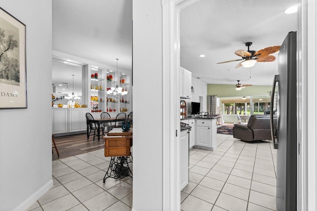 interior space with a textured ceiling, light tile patterned flooring, white cabinets, ceiling fan, and stainless steel fridge