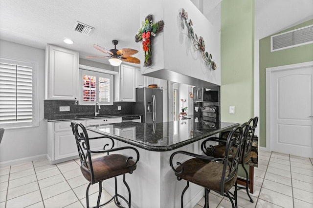 kitchen with a breakfast bar, white cabinets, backsplash, ceiling fan, and stainless steel fridge with ice dispenser