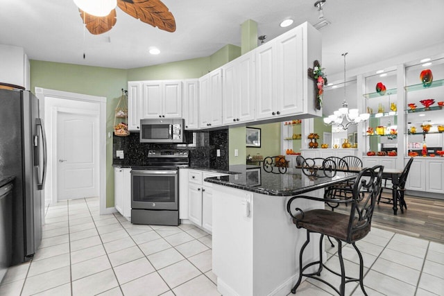 kitchen featuring white cabinetry, kitchen peninsula, stainless steel appliances, a kitchen bar, and ceiling fan