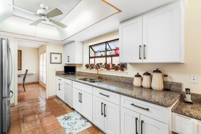 kitchen with white dishwasher, stainless steel fridge, white cabinetry, and sink