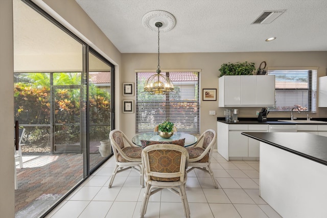 dining room with an inviting chandelier, a textured ceiling, sink, and light tile patterned flooring