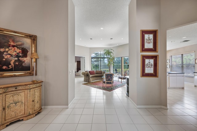 corridor featuring a high ceiling, light tile patterned floors, and a textured ceiling