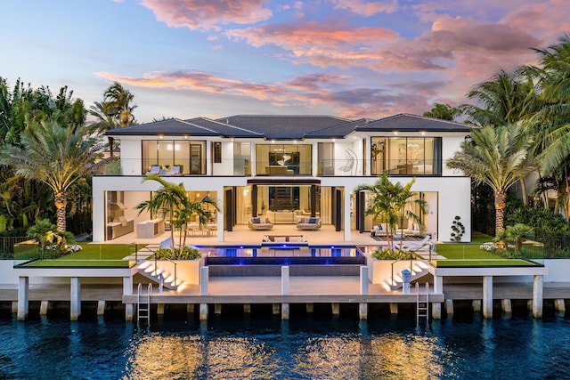 back house at dusk featuring a lawn, a patio, and a water view