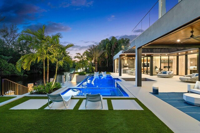 pool at dusk featuring ceiling fan, a yard, and a patio area