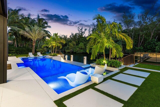 pool at dusk featuring a water view and a patio area