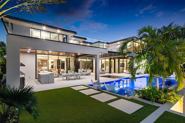 back house at twilight featuring outdoor lounge area, a lawn, and a patio