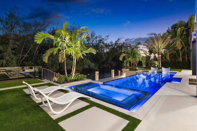 pool at dusk with a patio and an in ground hot tub