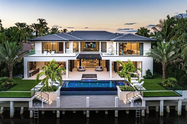 back house at dusk featuring a lawn, a patio, a swimming pool with hot tub, and a bar