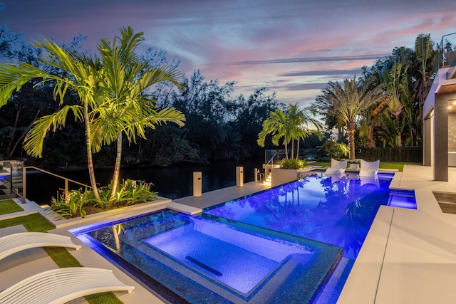 pool at dusk with a patio and an in ground hot tub