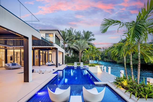 pool at dusk with a patio, a water view, and an outdoor living space