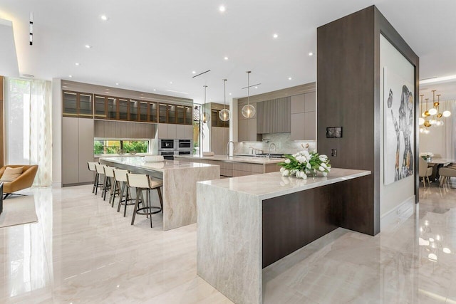 kitchen featuring a large island, sink, a kitchen breakfast bar, decorative light fixtures, and light stone countertops