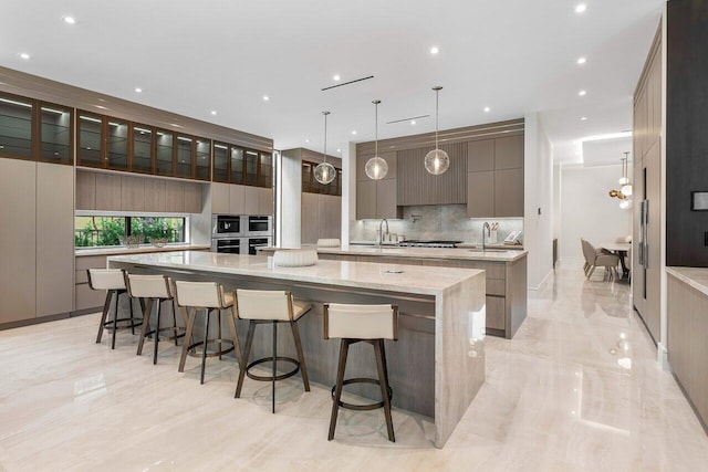 kitchen with a large island, a breakfast bar, light stone counters, pendant lighting, and sink