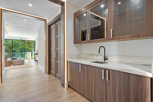 bar featuring light wood-type flooring, dark brown cabinets, sink, and light stone counters