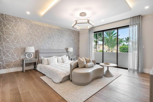 bedroom featuring a tray ceiling, light hardwood / wood-style flooring, and access to exterior