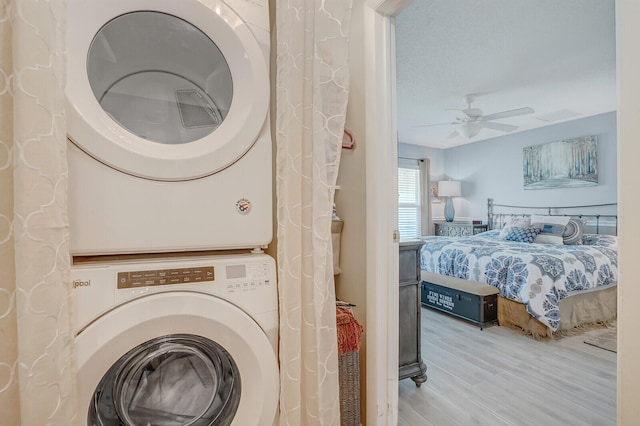 clothes washing area featuring light wood-type flooring, ceiling fan, and stacked washer and clothes dryer