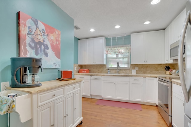 kitchen featuring white cabinets, sink, tasteful backsplash, appliances with stainless steel finishes, and light hardwood / wood-style floors