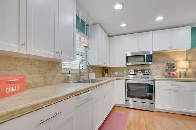 kitchen with appliances with stainless steel finishes, light hardwood / wood-style floors, white cabinetry, tile counters, and sink