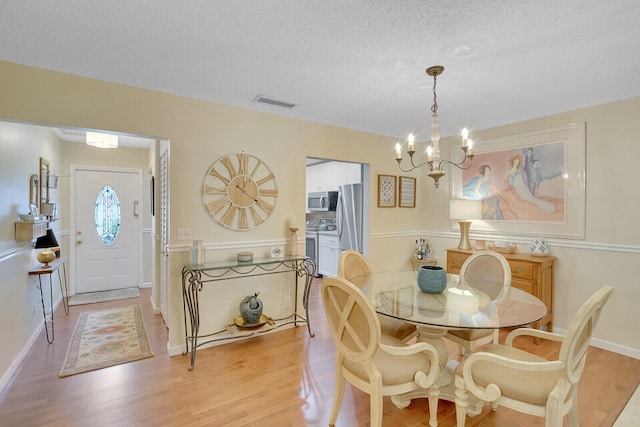 dining area with a textured ceiling, light hardwood / wood-style flooring, and a chandelier