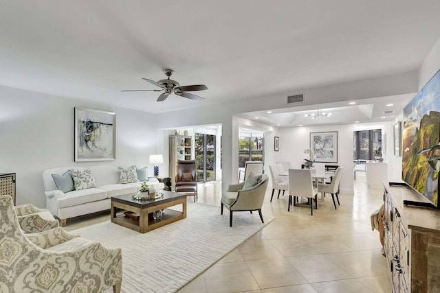 living room featuring ceiling fan, a tray ceiling, and light tile patterned floors