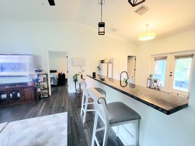 kitchen with decorative light fixtures, dark countertops, visible vents, vaulted ceiling, and a kitchen breakfast bar