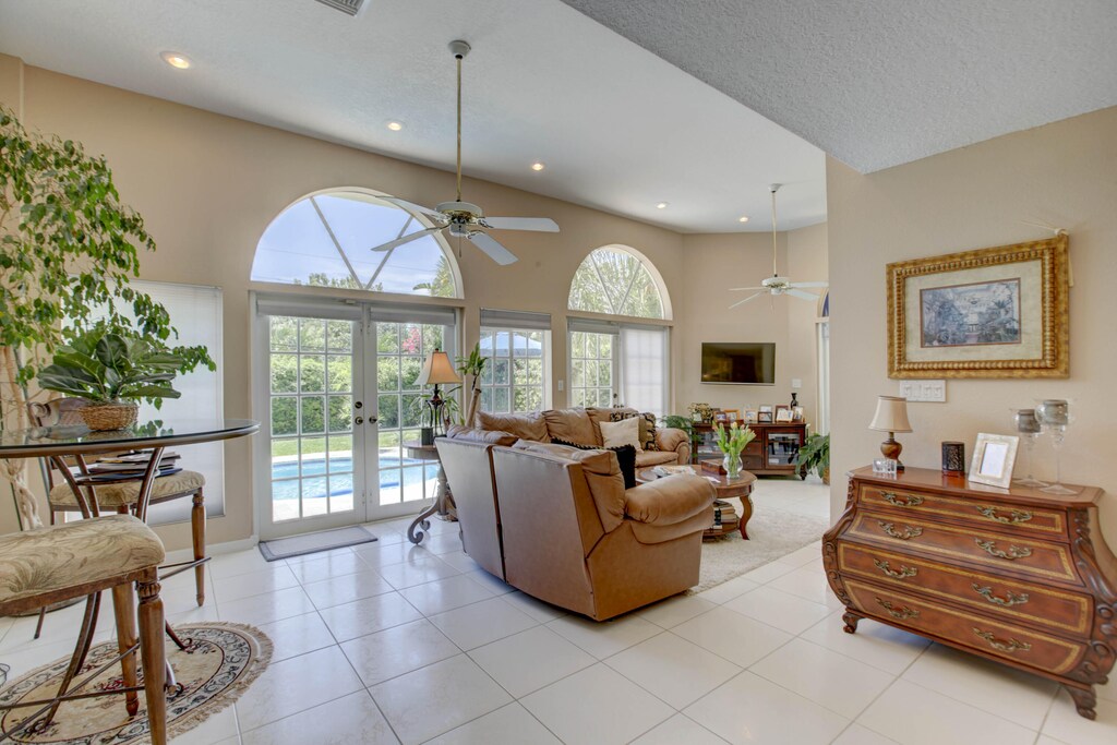 living room featuring light tile patterned floors, french doors, a towering ceiling, and a ceiling fan