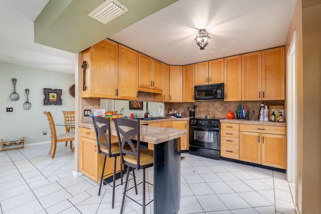 kitchen featuring black appliances, a kitchen bar, decorative backsplash, and light tile patterned floors