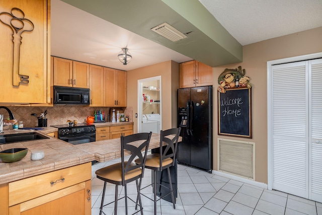 kitchen with sink, black appliances, tile countertops, a breakfast bar, and separate washer and dryer